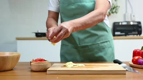 Closeup of hands slicing fresh garlic on a wooden cutting board in kitchen... Video stock 312979164