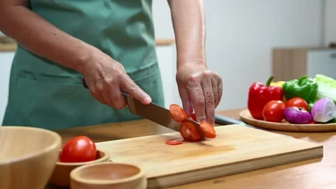 Closeup of hands slicing tomato with a sharp knife on wooden board in kitch.. Stock Footage 312978899