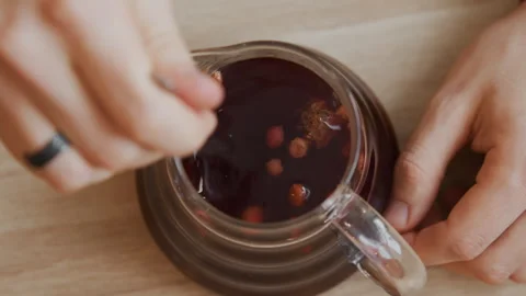 Closeup of hands stirring dark liquid in transparent glass pitcher on wooden Stock Footage 345729826