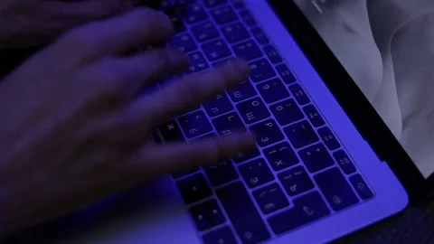 Closeup hands typing on laptop keyboard under blue light and screen turns on Stock Footage 229705944