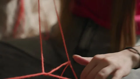 Closeup hands weaving red yarn into pattern on lap, casual clothing, sunlit room Stock Footage 323311487