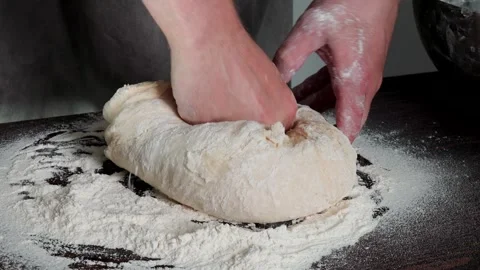 Closeup of hands working pliable dough on floured surface dark table and kitchen Stock Footage 310337323