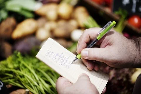 Closeup of hands writing vegetable list on notebook Stock Photos