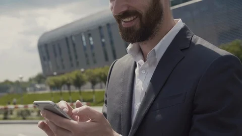 CloseUp of Handsome Bearded Man using his Smartphone near Office Building Stock Footage 113276882