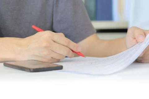 Closeup human hand checking work on a paper. freelance man writing with red p Stock Photos