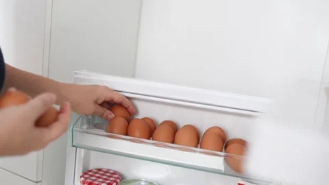 Closeup human hands put chicken eggs in egg-laying compartment in refrigerator Stock Footage 251637142