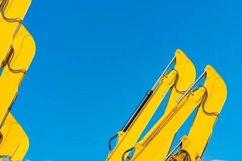 Closeup hydraulic piston of yellow backhoe against blue sky. Heavy machine fo 库存照片