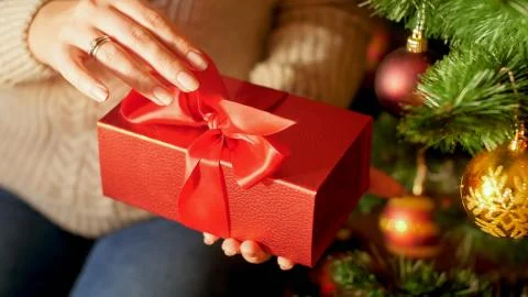 Closeup image of female hands pulling red ribbon and opening Christmas present Foto stock