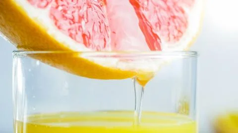 Closeup image of fresh juice dripping from grapefruit slice in glass Stock Photos