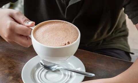 Closeup image of hands holding a cup of hot chocolate on rustic wooden back.. Stock Photos