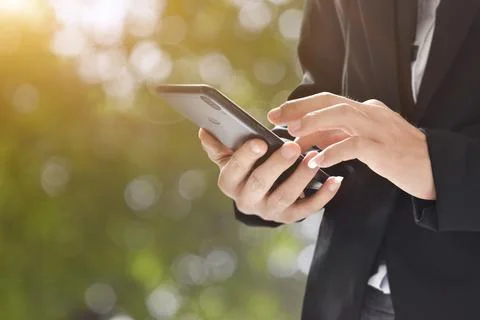 Closeup image of man holding and using mobile phone on bokeh background outdo Stock Photos