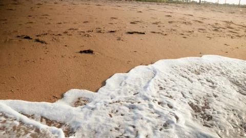 Closeup image of sea waves rolling over dirty sand on the deserted beach at Stock Photos