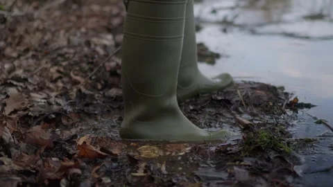 A closeup image showing green rubber boots stepping through brown muddy water Video stock 305496595