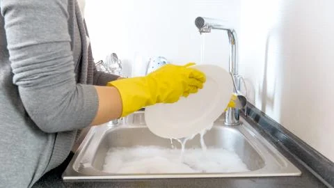 Closeup image of young woman in latex protective gloves washing dishes under Stock Photos