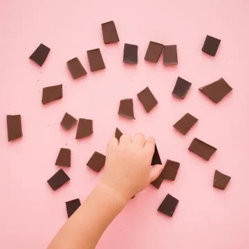 Closeup of kid boy hand taking a piece of chocolate from pink table backgroun Stock Photos