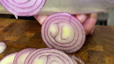 Closeup of a knife slicing red onion into thin rings on a wooden cutting bo.. Video stock 346600625
