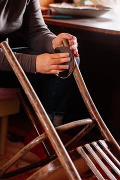Closeup of lady sitting sanding surface of aged stool in need of renovation with Stock Photos