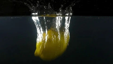 Closeup of a lemon falling into water on the black background slow motion Stock Footage 75790264