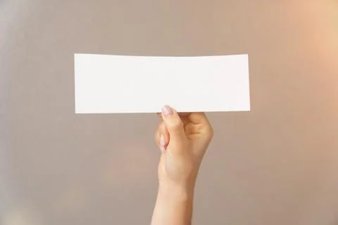 Closeup on a light background a womans hand holds white paper for text inscri Stock Photos