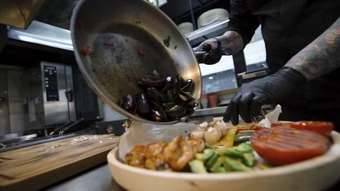 Closeup low angle shot of chef putting mussels in dishes with grilled vegetables Видео 105272034