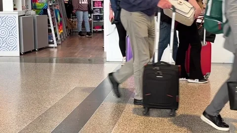 Closeup of luggage being pulled by passengers walking thru busy airport terminal Stock Footage 256246620