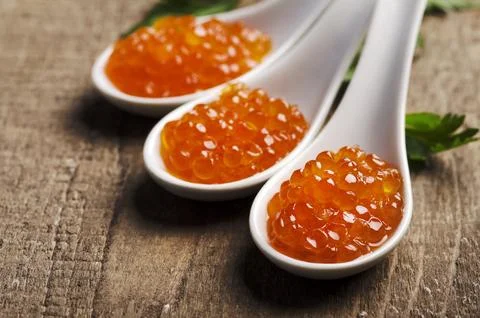 Closeup of luxury red caviar in white spoon with parsley on wooden table ba.. Foto stock