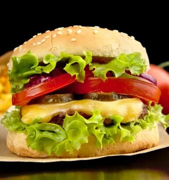 Closeup macro shot of big cheeseburger on paper on wooden black desk Stock Photos