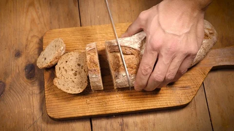 Closeup of male hands cutting bread slices on a wooden board Stock Footage 121129820
