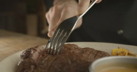 Closeup of male hands using knife and fork while cutting beef steak on grill Stock Footage 103672676