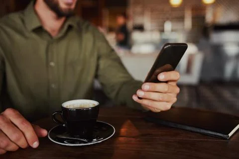 Closeup of male hands using mobile phone drinking coffee while sitting in Stock Photos