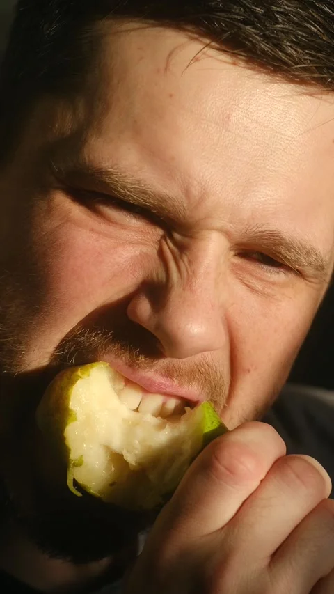 Closeup of man biting pear, Gritty portrait showing man chewing fruit intensely Video stock 337547024