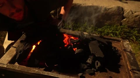 Closeup a man blowing into the coals of a china box to start the fire throwing s Stock Footage 199528283