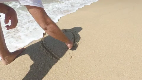 Closeup of man drawing a heart on the beach sand and sea wave covering Stock Footage 171374059