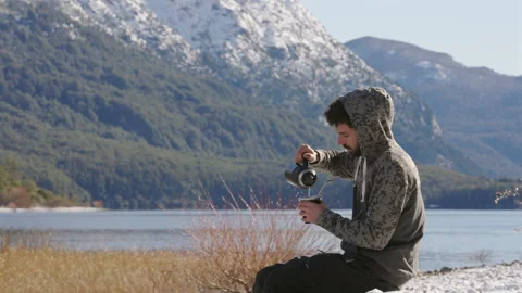 Closeup of man drinking Yerba Mate on log by a lake in Patagonia during winter Stock Footage 327443826