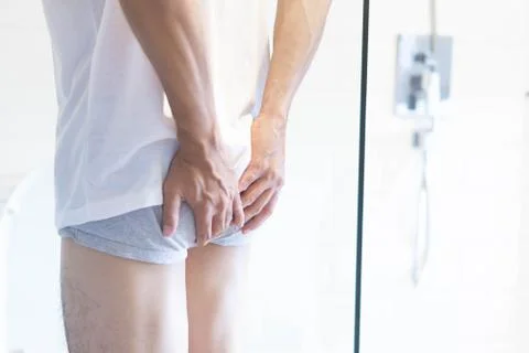 Closeup man holding bladder with pee pain in the toilet, selective focus Stock Photos