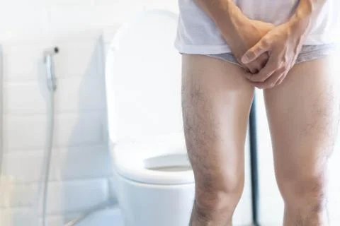 Closeup man holding bladder with pee pain in the toilet, selective focus Stock Photos