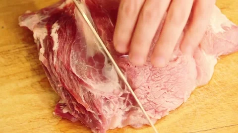 Closeup man in the kitchen is cutting pork on cutting board Stock Footage 65429791
