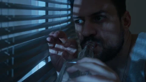 Closeup Man Looking Through Blinds at Night and Drinking Alcohol 動画素材 311504120