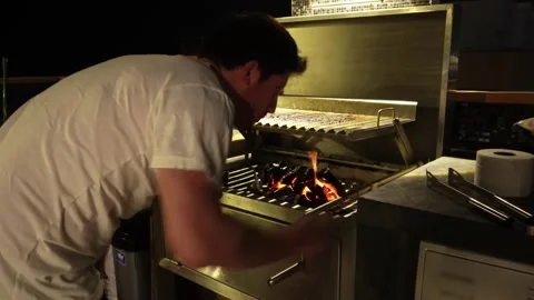 Closeup of a man moving red hot coals from a grill with a fork and hands to cook Stock Footage 173514810