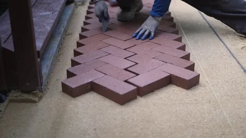 Closeup of man putting trowel between red brick pavers in a herringbone pattern Stock Footage 82093495