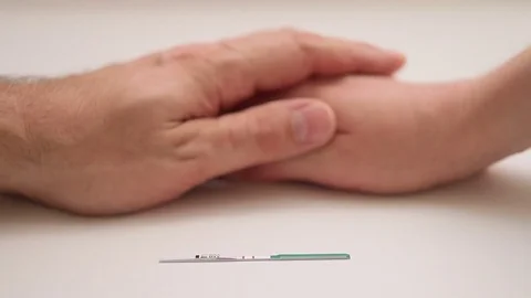 Closeup of a man stroking a woman's hand, next is a pregnancy test with a Stock Footage 81874088