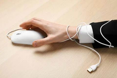 Closeup of man taking computer mouse at wooden table, hand tied with cable. I Stock Photos