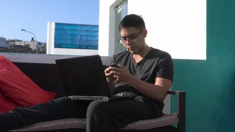 Closeup of a man telecommuting from a beach house with his laptop and cell phone 库存影片 155825543