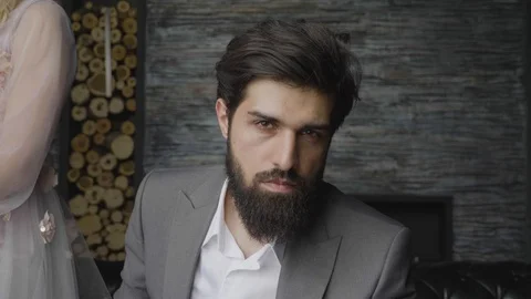 Closeup man with thick beard sits looks into camera by wall Stock Footage 103925121
