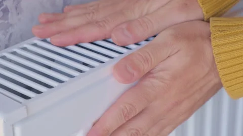 Closeup of man warming his hands in yellow sweater on the heater at home 動画素材 231236970
