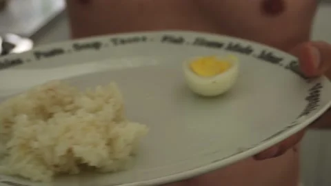 Closeup of a man without polo serving rice on a plate with a boiled egg in the Vidéo 189100717