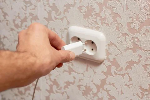 Closeup of a man's hand inserting an electrical plug into a wall socket. Stock Photos