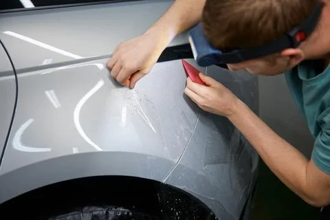 Closeup master hand with rubber scraper applying sticking protective film on car Stock Photos