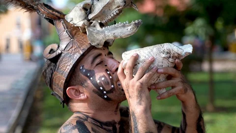 Closeup of a Mayan or Aztec dancer musician blowing into a conch shell as Stock Footage 126991130