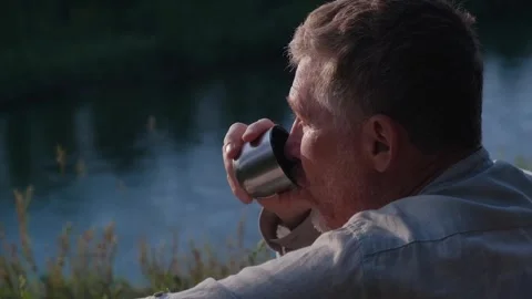 Closeup middle aged man drinks tea from mug on the riverbank. relax and travel. Stock Footage 264208849
